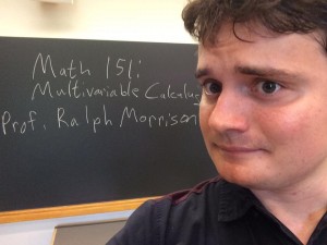 Ralph Morrison in front of a chalkboard with the text "Math 151:  Multivariable Calculus, Prof. Ralph Morrison" written on it