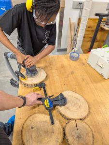 Divine Uwimana ‘27 sands the circular wood slices to prepare them for their laser engravings.