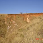 Red laterite above tan and white saprolite in vertical headwall of lightly active stage III lavaka