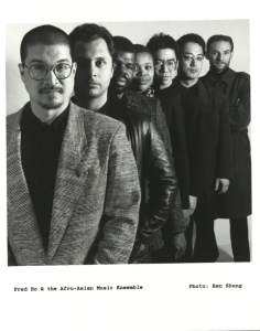 The photograph shows a black and white image of Fred Ho on the far left along with the Afro-Asian Music Ensemble next to him. The photo was taken by Ken Shung.